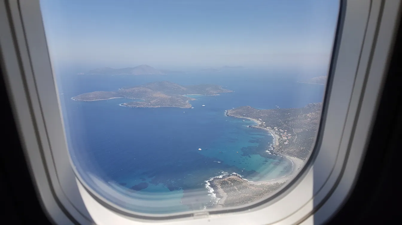 Der Blick aus dem Flugzeugfenster zeigt eine atemberaubende Aussicht auf die griechischen Inseln, umgeben von tiefblauem Meer, ideal für einen Strandurlaub auf Korfu. Die Inselgruppe ist von der Luft aus gut sichtbar, während das Flugzeug auf dem Hinflug nach Korfu (CFU) in Richtung seines Ziels fliegt.